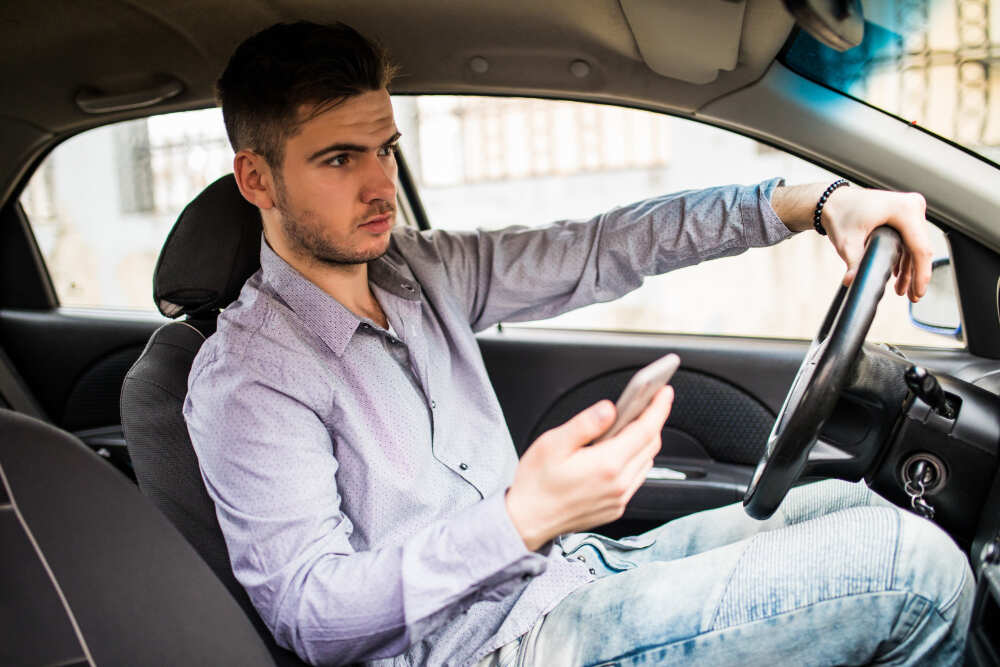 Young man looking at mobile phone while driving a car
